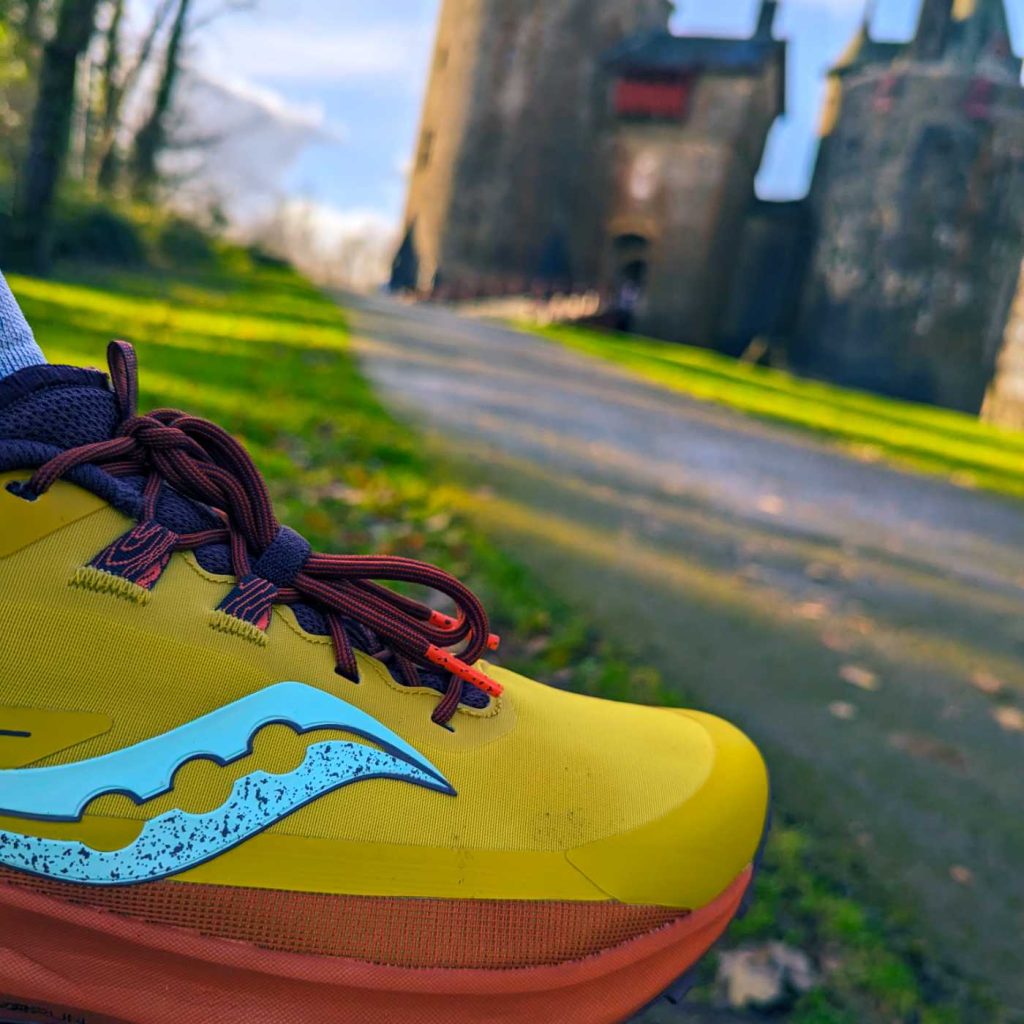 A yellow and orange trail running shoe with Castell Coch in the distance