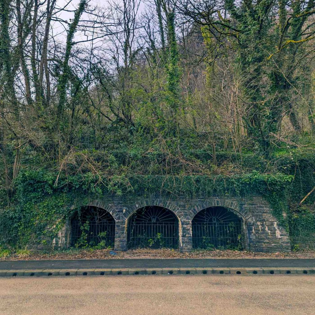 Three stone arches on the side of a road covered in ivy