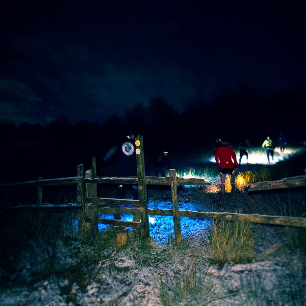 Trail runners climbing over a stile on a snowy hill.